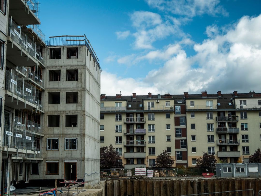 Mehrgeschossiger Rohbau neben fertigen Wohnhäusern unter blauem Himmel